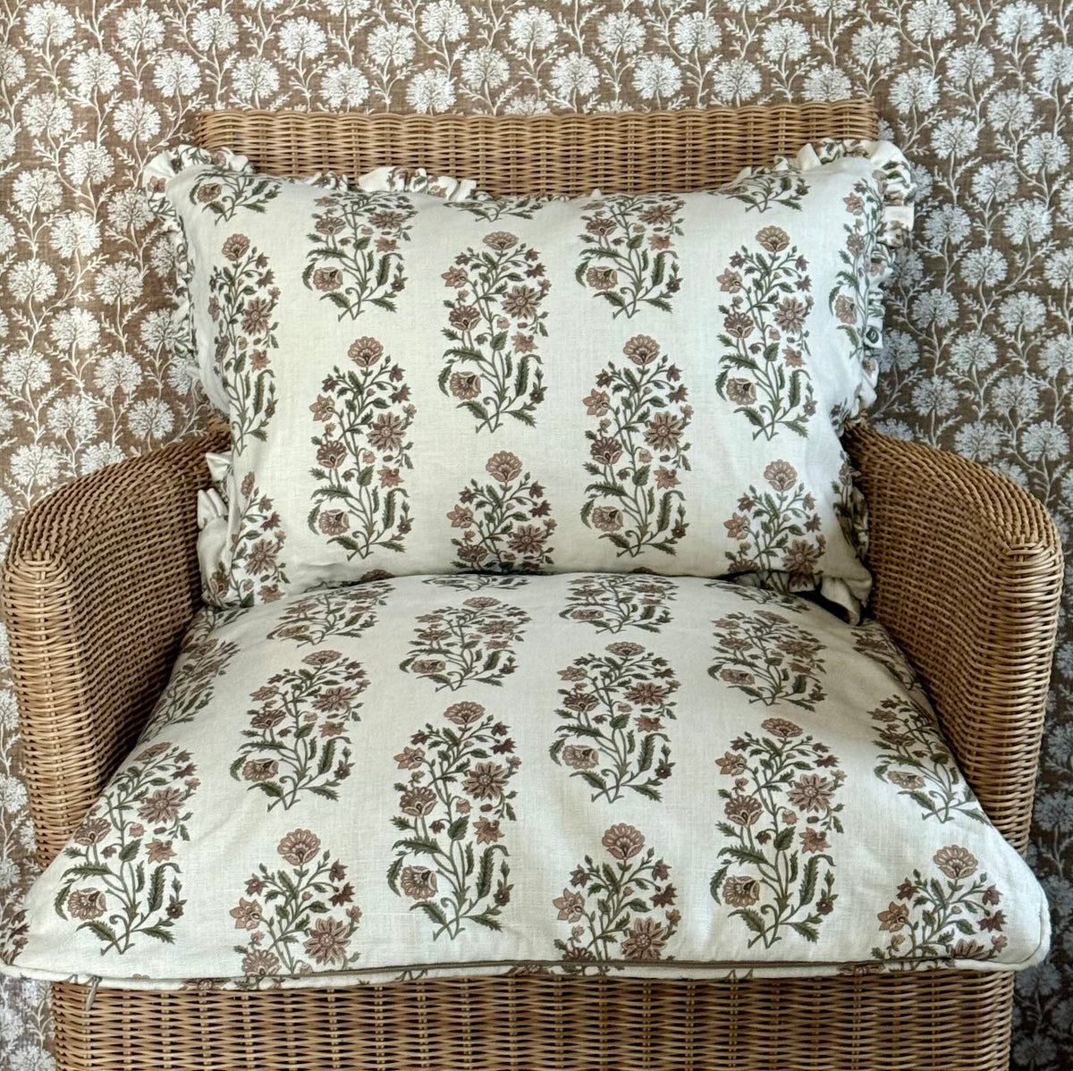 Wicker chair with floral-patterned San Marino  cushions against a floral Brynn pattern wallpapered wall.