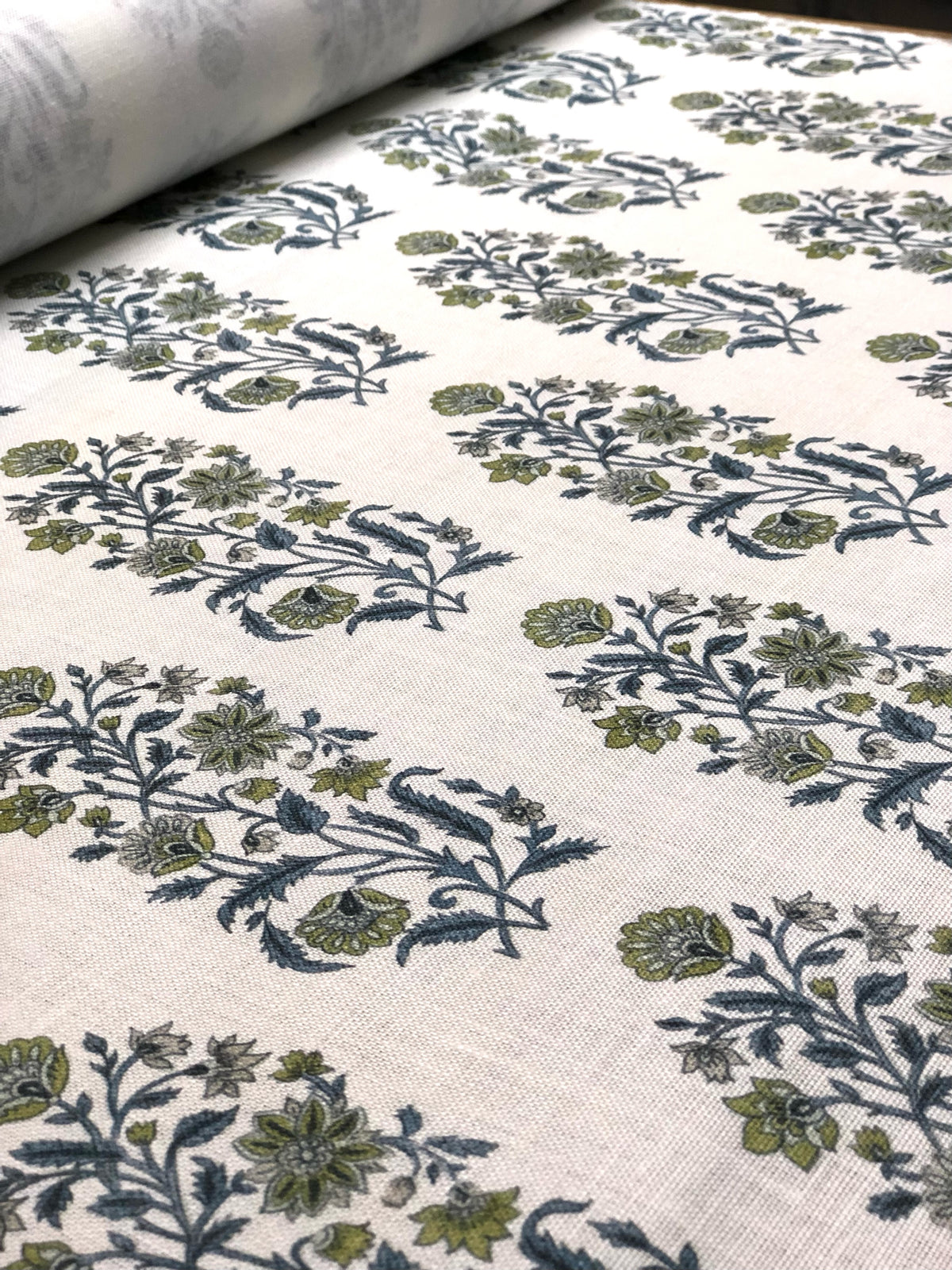 A San Marino textile print detail on a roll a floral pattern in various colors, predominantly blue and green, with a white linen background