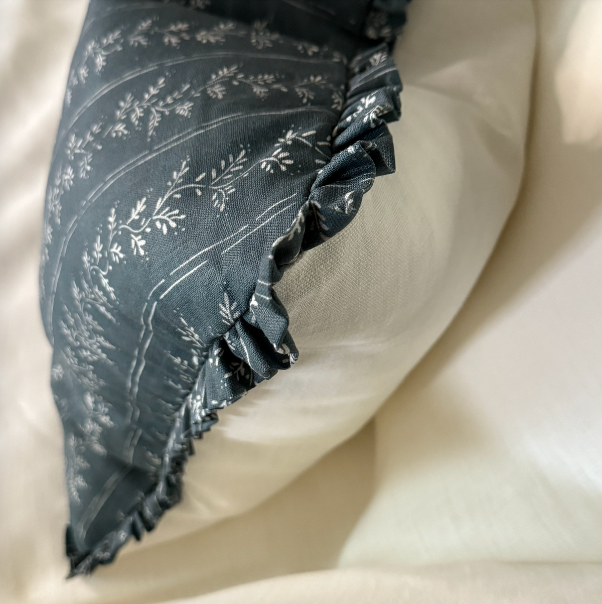 Dark floral-patterned pillow with ruffles on a light ivory linen background